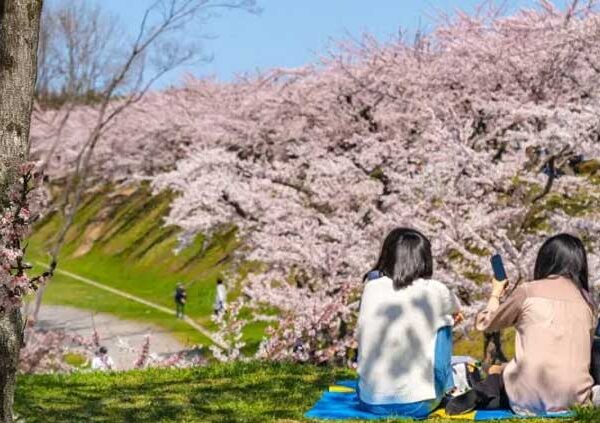 Jardim de Primavera simbolizando a Golden Week. Duas mulheres sentadas na grama contemplando a paisagem.