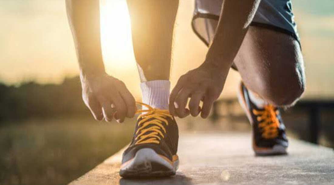 Atleta amarrando o tênis na pista de corrida no final da tarde.