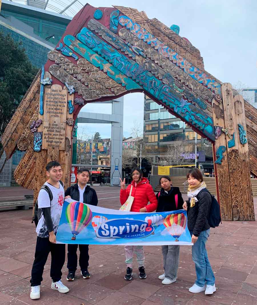 Alunos da Spring School segurando a bandeira da escola em frente ao Auckland Zoo.