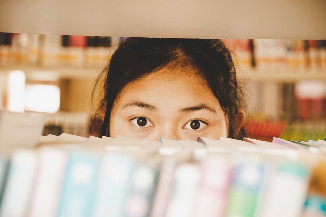 Aluna oriental na entre as prateleiras de livros na biblioteca.