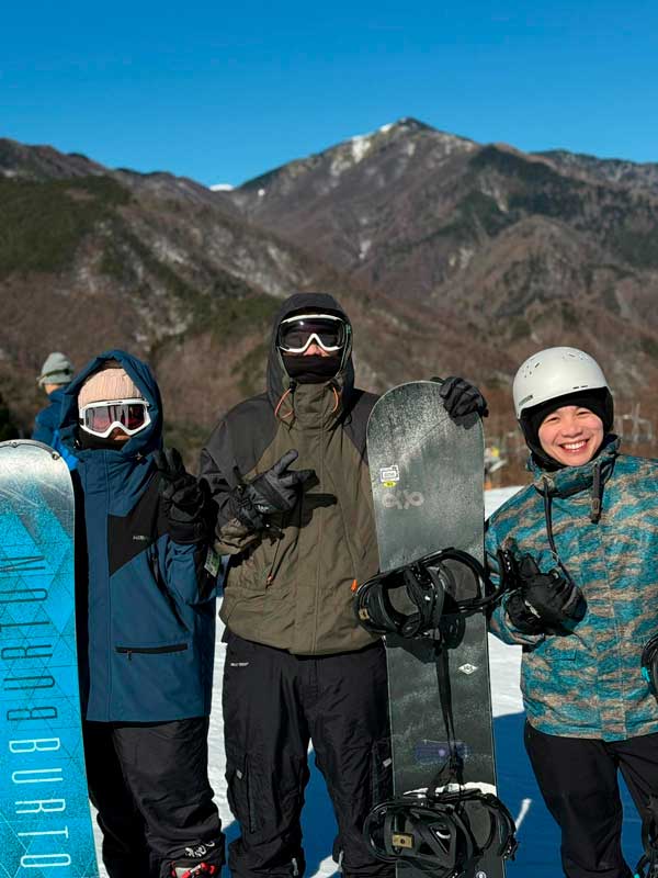 Três membros da Spring School com roupa de neve e prancha de wakeboard ao lado.
