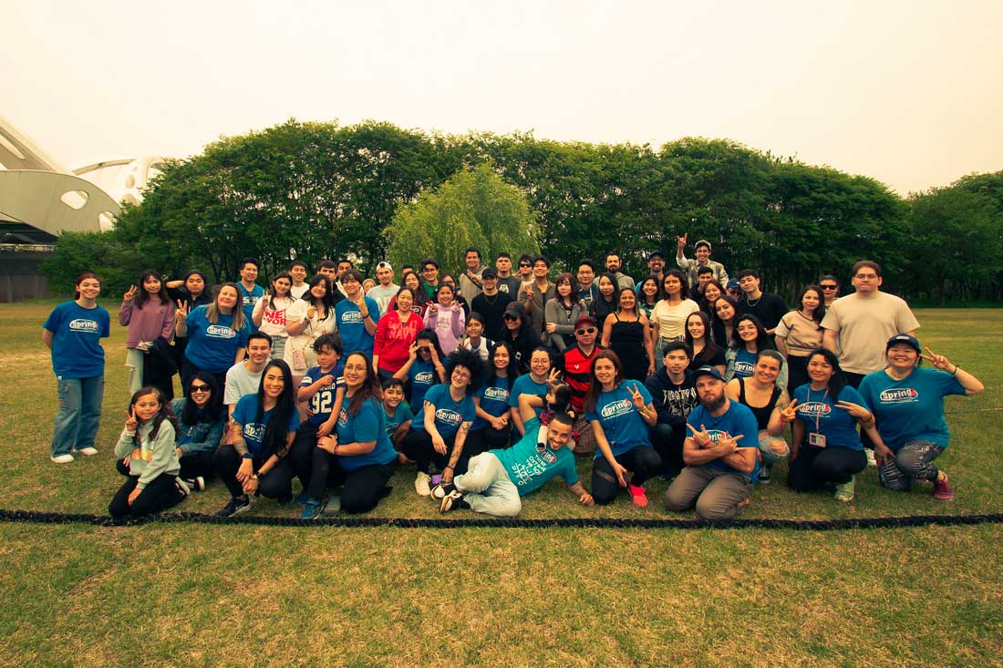 Alunos e Equipe Spring School pousando para foto em belo jardim gramado e com árvores ao fundo.